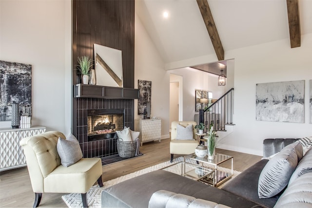 living room with beamed ceiling, high vaulted ceiling, light wood-type flooring, and a tile fireplace