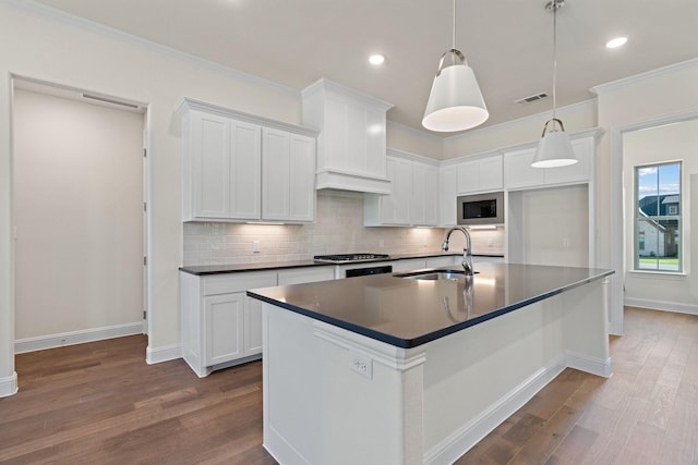 kitchen with built in microwave, sink, decorative light fixtures, white cabinetry, and an island with sink