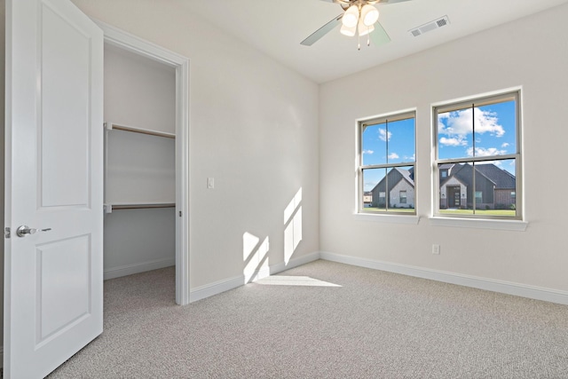 unfurnished bedroom with a walk in closet, light carpet, ceiling fan, and a closet