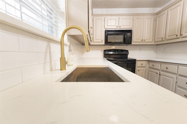 kitchen featuring light stone countertops, decorative backsplash, a textured ceiling, sink, and black appliances