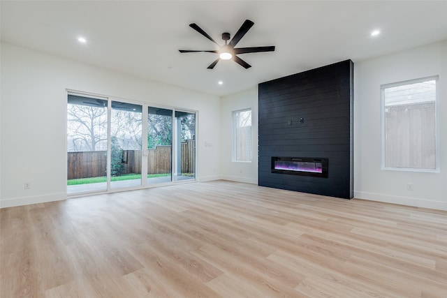 unfurnished living room featuring ceiling fan, a large fireplace, and light hardwood / wood-style floors