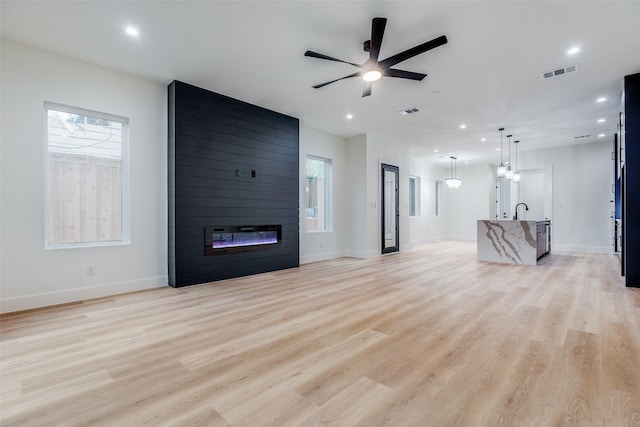 unfurnished living room with ceiling fan, light wood-type flooring, and a fireplace