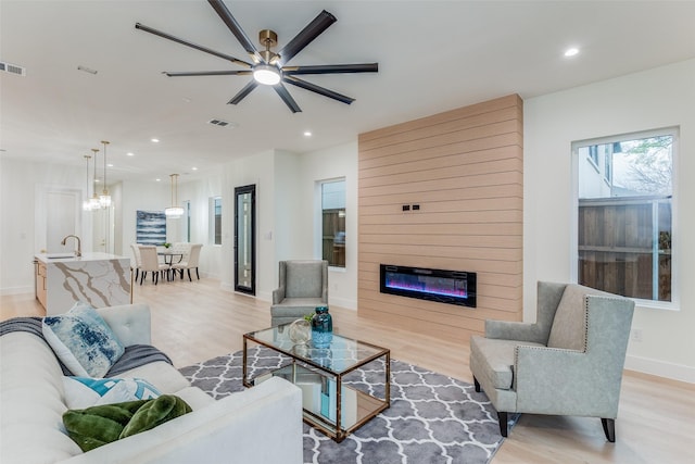 living room with a large fireplace, light hardwood / wood-style floors, ceiling fan, and sink