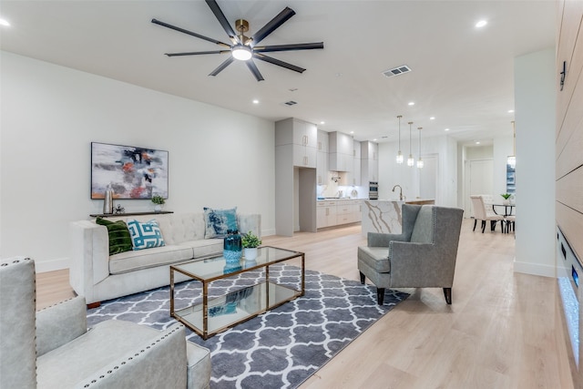 living room featuring ceiling fan, sink, and light wood-type flooring