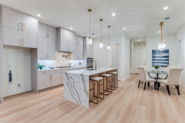 kitchen featuring stainless steel appliances, an island with sink, light hardwood / wood-style floors, decorative light fixtures, and decorative backsplash