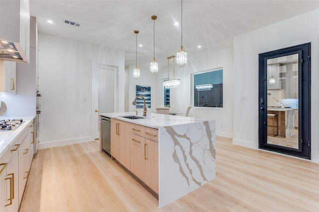 kitchen featuring light brown cabinets, sink, hanging light fixtures, light stone countertops, and an island with sink