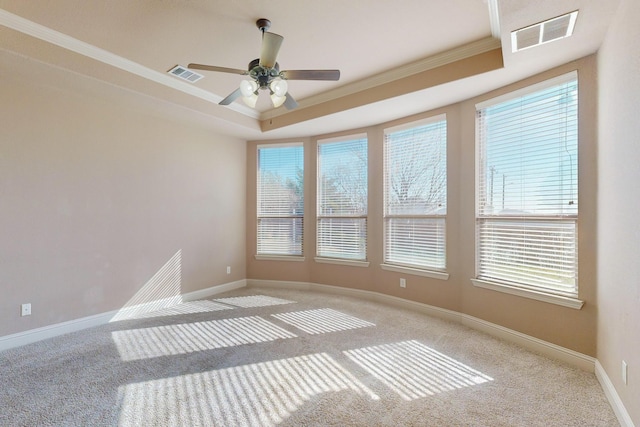 carpeted empty room featuring ceiling fan, plenty of natural light, ornamental molding, and a tray ceiling