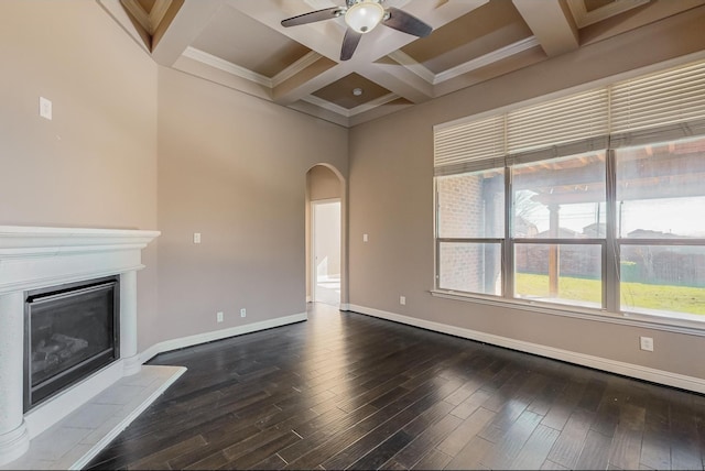 unfurnished living room featuring a tile fireplace, dark wood-type flooring, coffered ceiling, beamed ceiling, and crown molding