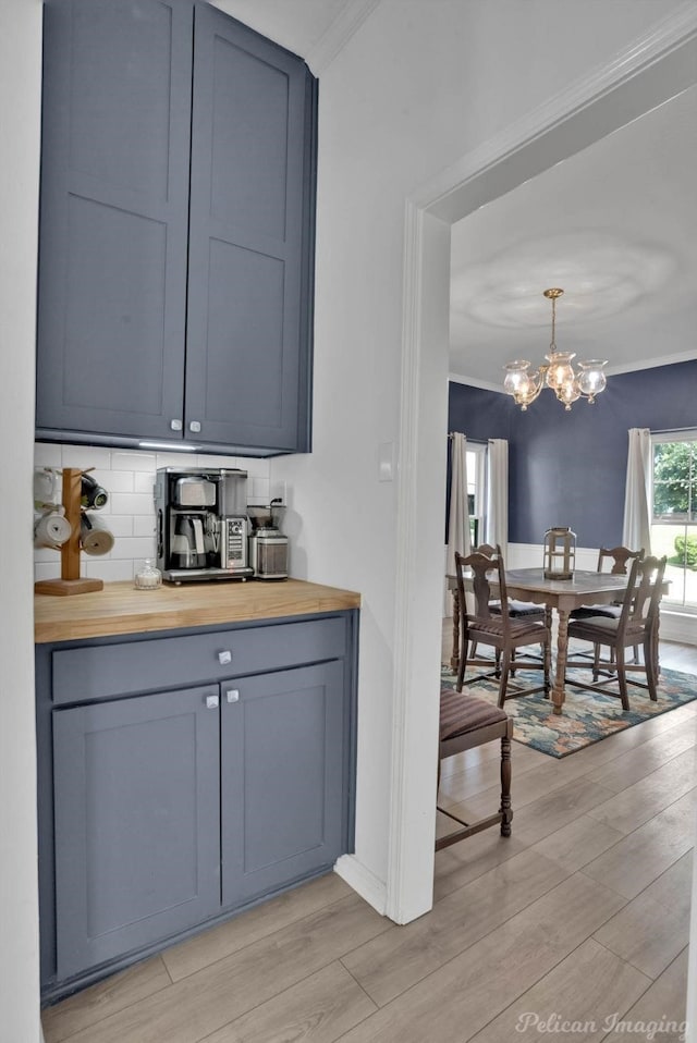 bar with decorative backsplash, light wood-type flooring, a notable chandelier, and wood counters