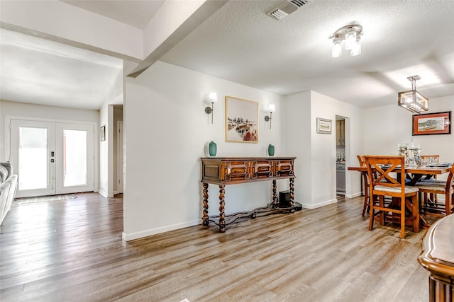 dining space with french doors, a textured ceiling, and light hardwood / wood-style flooring