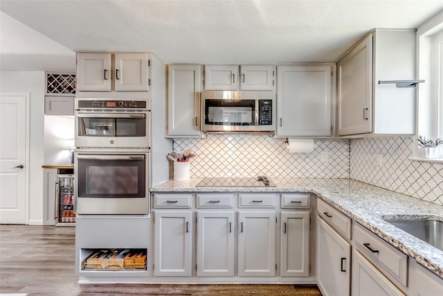 kitchen featuring appliances with stainless steel finishes, light wood-type flooring, tasteful backsplash, light stone counters, and a textured ceiling