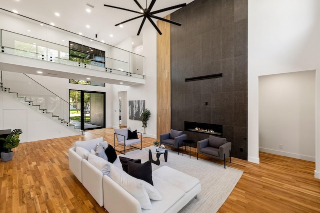 living room with a tiled fireplace, french doors, a high ceiling, and light wood-type flooring