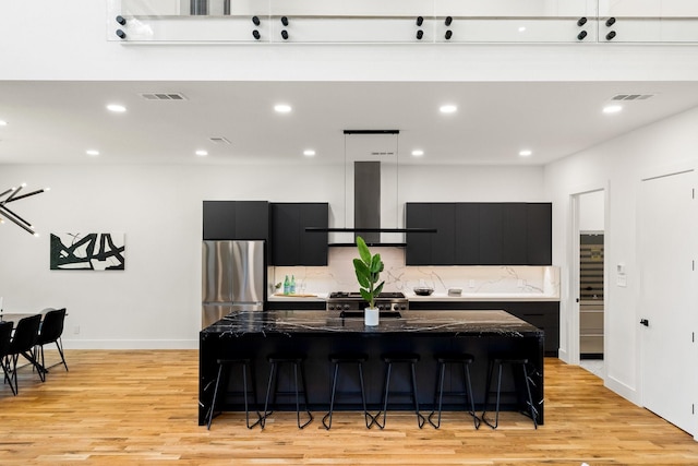 kitchen featuring stainless steel refrigerator, ventilation hood, stove, a kitchen island with sink, and a breakfast bar