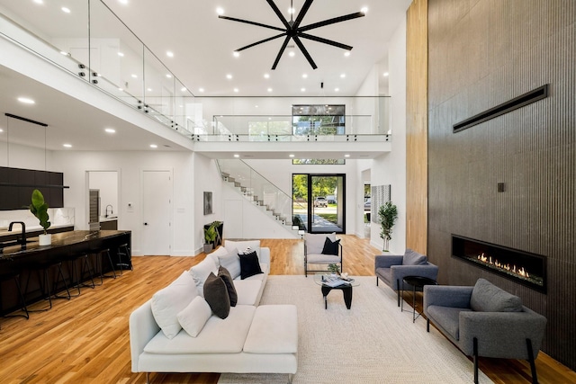 living room with a fireplace, a towering ceiling, an inviting chandelier, and light wood-type flooring