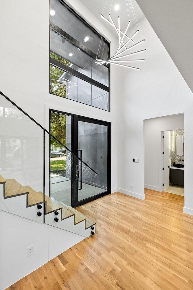 foyer entrance with wood-type flooring, a towering ceiling, and a chandelier