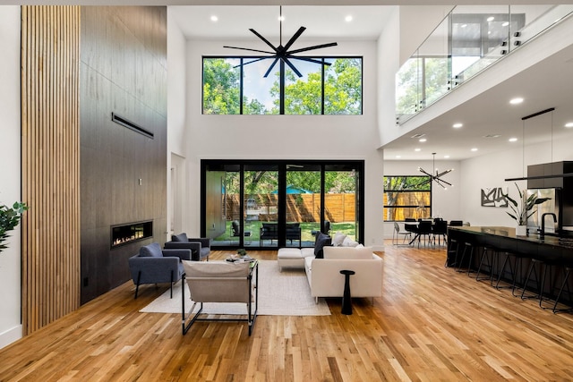 living room with a fireplace, light hardwood / wood-style flooring, a high ceiling, and an inviting chandelier