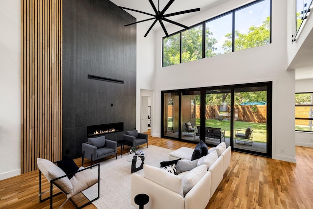 living room featuring ceiling fan, light wood-type flooring, a towering ceiling, and a fireplace