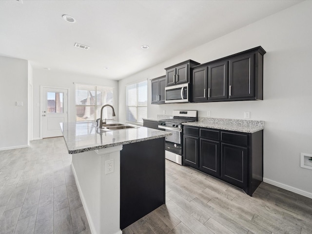 kitchen featuring light stone countertops, sink, light hardwood / wood-style flooring, a center island with sink, and appliances with stainless steel finishes