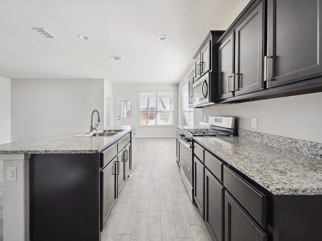 kitchen with appliances with stainless steel finishes, sink, light stone counters, and an island with sink