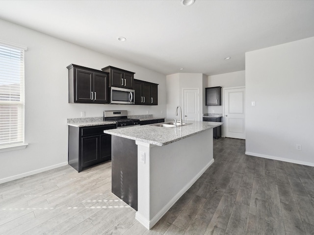 kitchen with a center island with sink, sink, stainless steel appliances, and hardwood / wood-style flooring