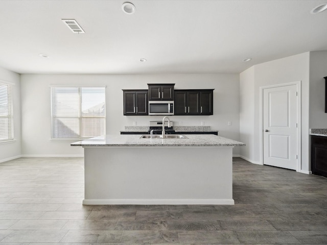 kitchen featuring light stone counters, dark hardwood / wood-style flooring, sink, and a kitchen island with sink