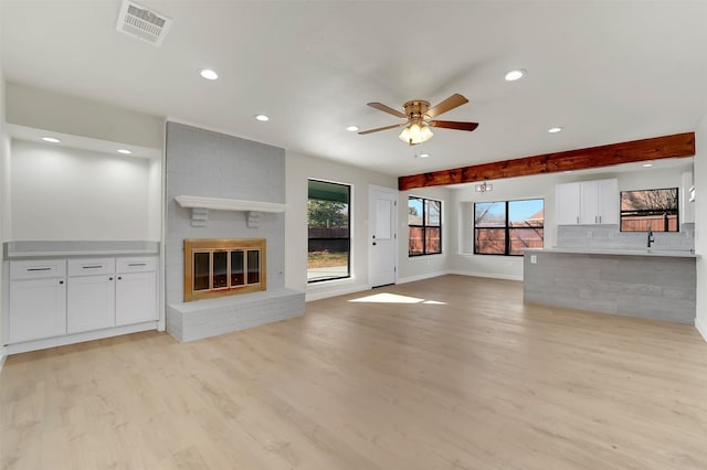 unfurnished living room with ceiling fan, light hardwood / wood-style flooring, beamed ceiling, and a brick fireplace