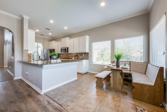 kitchen with stainless steel appliances, backsplash, kitchen peninsula, white cabinets, and ornamental molding