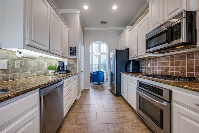 kitchen featuring tasteful backsplash, dark stone counters, stainless steel appliances, crown molding, and white cabinets