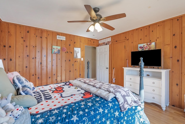 bedroom featuring ceiling fan, light hardwood / wood-style floors, and wood walls