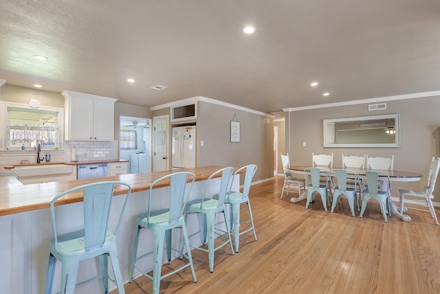 kitchen with a breakfast bar, sink, white cabinetry, white fridge, and butcher block counters