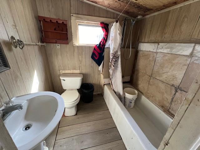 full bathroom with sink, hardwood / wood-style flooring, wooden walls, shower / bath combination with curtain, and toilet