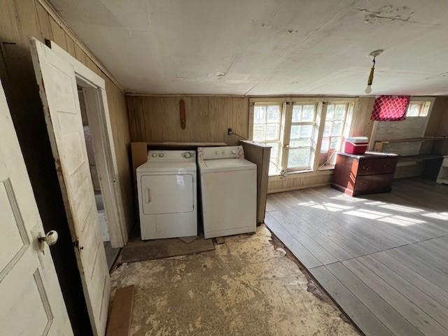 laundry area with washing machine and dryer, light hardwood / wood-style flooring, and wood walls