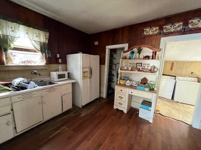 kitchen featuring white appliances, white cabinetry, wooden walls, washing machine and dryer, and dark hardwood / wood-style floors