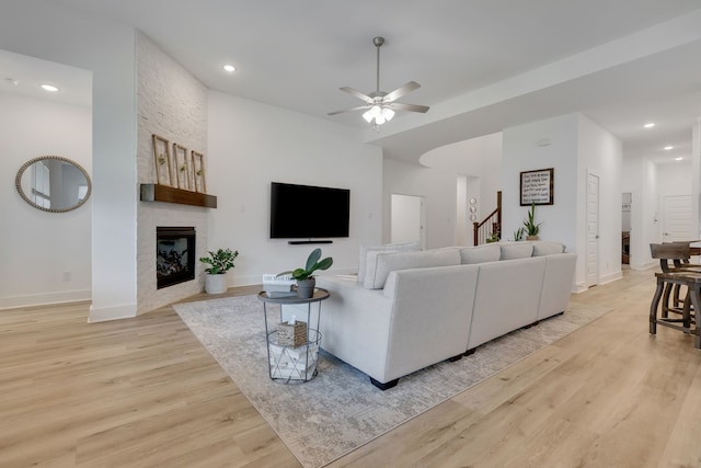 living room featuring ceiling fan, a large fireplace, and light wood-type flooring