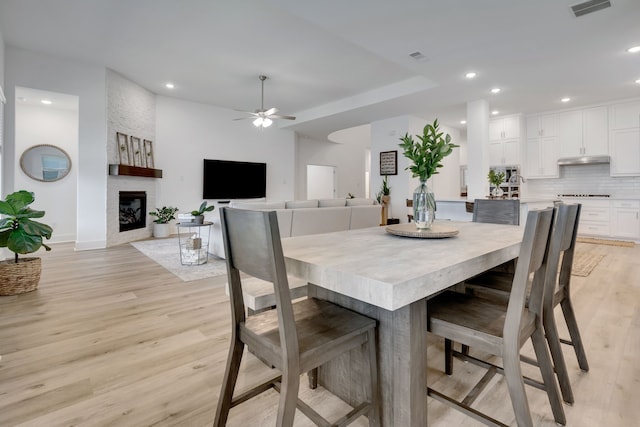 dining room with ceiling fan, a large fireplace, and light wood-type flooring