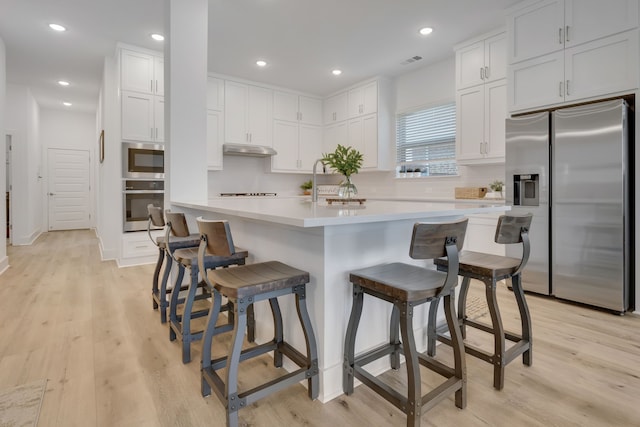 kitchen featuring a kitchen breakfast bar, white cabinetry, stainless steel appliances, and light wood-type flooring