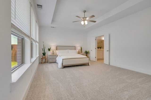 carpeted bedroom featuring a raised ceiling, ensuite bath, ceiling fan, and multiple windows