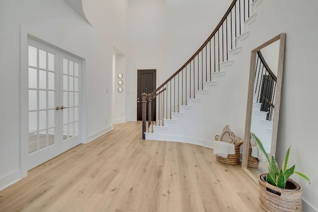 foyer entrance featuring light hardwood / wood-style floors, a towering ceiling, and french doors