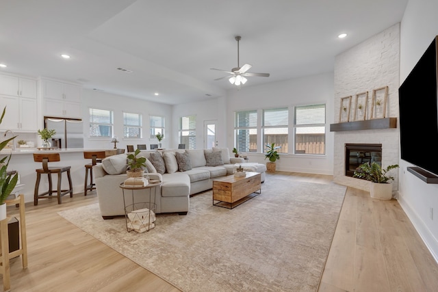 living room with ceiling fan, light wood-type flooring, and a fireplace