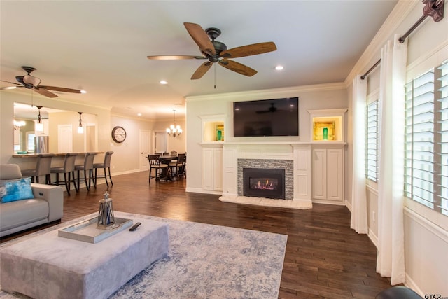 living room featuring a fireplace, dark wood-type flooring, ceiling fan with notable chandelier, and ornamental molding