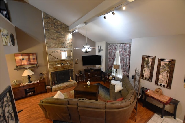 living room featuring light wood-type flooring, track lighting, ceiling fan, lofted ceiling with beams, and a fireplace