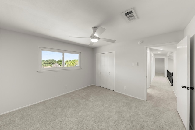 unfurnished bedroom featuring ceiling fan, a closet, and light carpet