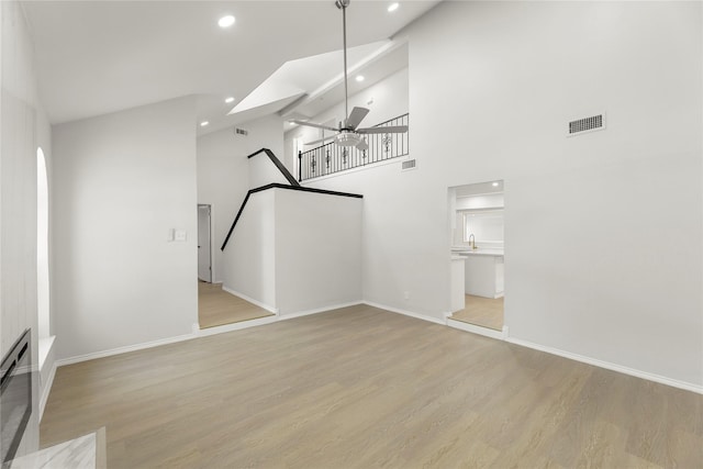 unfurnished living room featuring a high ceiling, light hardwood / wood-style flooring, and ceiling fan