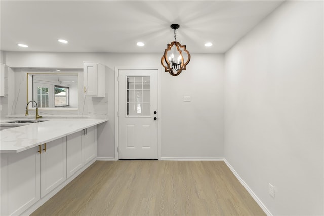 kitchen with sink, white cabinetry, decorative light fixtures, light hardwood / wood-style flooring, and light stone countertops