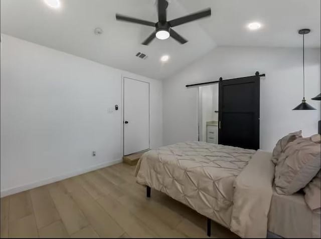 bedroom with a barn door, ceiling fan, light hardwood / wood-style flooring, and vaulted ceiling