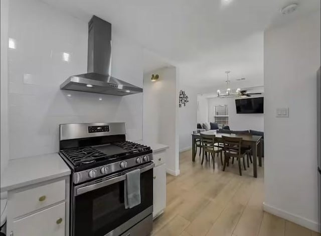 kitchen featuring gas stove, ceiling fan, wall chimney range hood, white cabinets, and light wood-type flooring