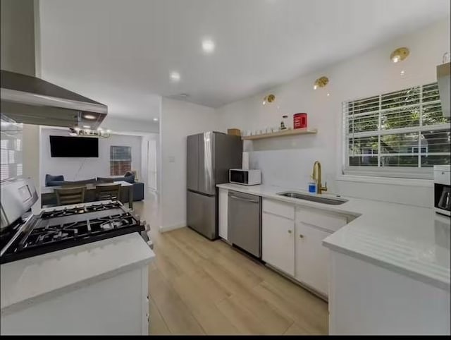 kitchen featuring stainless steel appliances, wall chimney range hood, sink, white cabinets, and light hardwood / wood-style floors