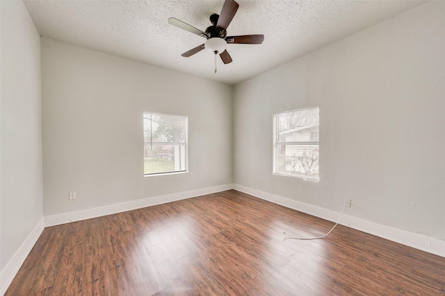 empty room with ceiling fan, dark hardwood / wood-style floors, a textured ceiling, and a wealth of natural light