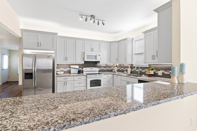 kitchen featuring tasteful backsplash, light stone counters, white appliances, and kitchen peninsula