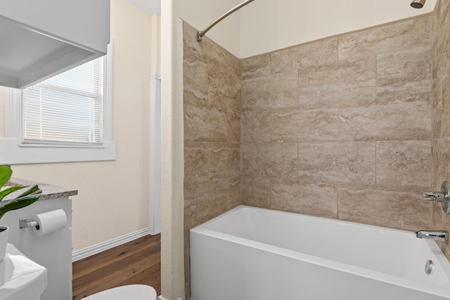 bathroom with wood-type flooring, toilet, and tiled shower / bath